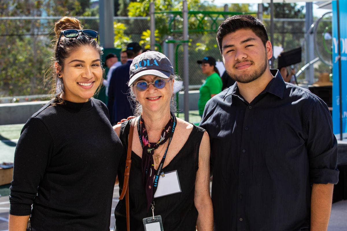 Leni Boorstin stands between two YOLA alumni at an outdoor event.