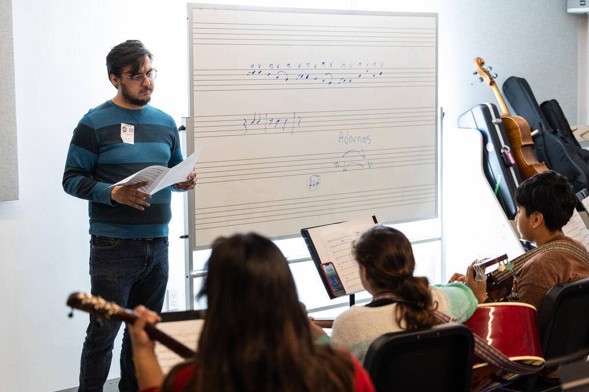 Instructor stands beside whiteboard with notes as students watch during a classroom presentation.
