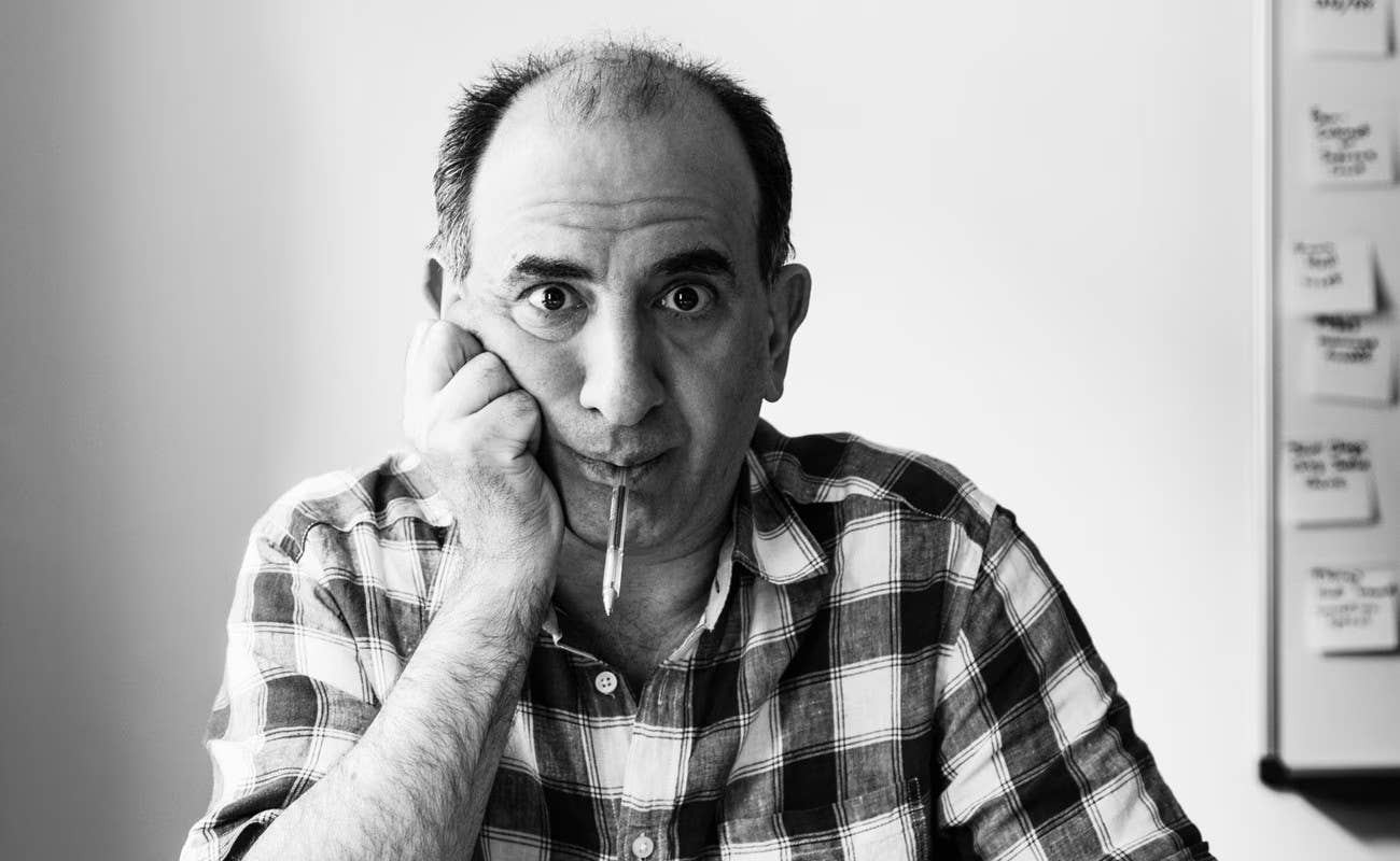 Black-and-white portrait of a man in a plaid shirt resting his chin on his hand, facing the camera.