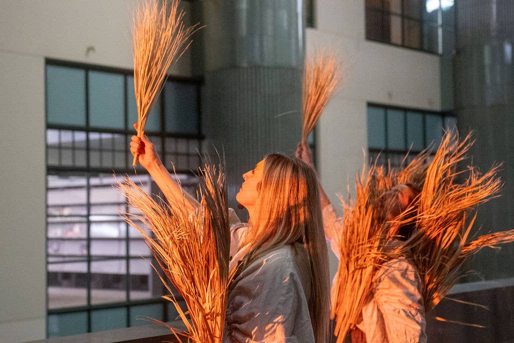 People carrying bright orange torches in a city courtyard, sparks catching light in front of modern buildings.