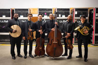 Orchestra musicians performing with violins and cellos in a concert hall, focused on sheet music stands.