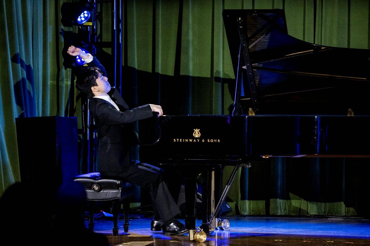 Pianist in a suit plays a Steinway grand piano under stage lights on a theater stage