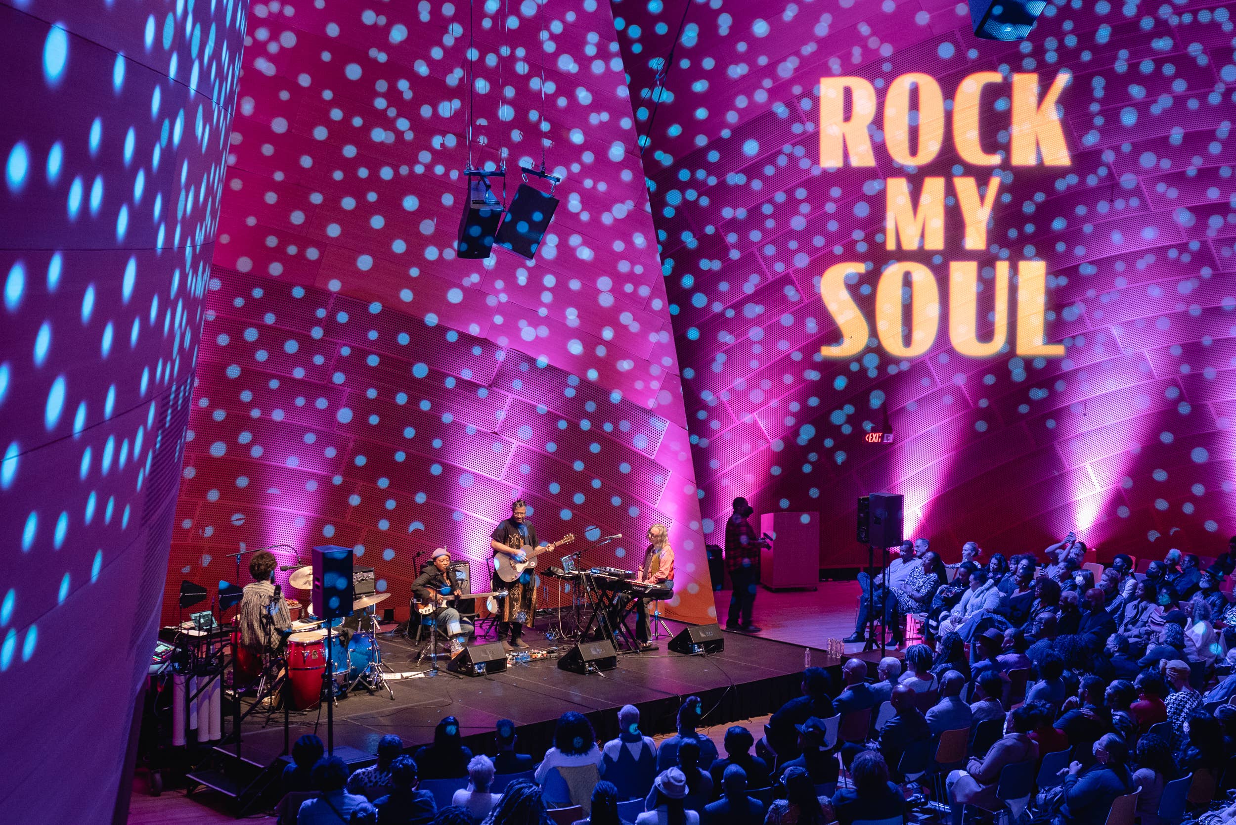 Concert stage with musicians under purple LED lights, with “Rock My Soul” text on the backdrop.