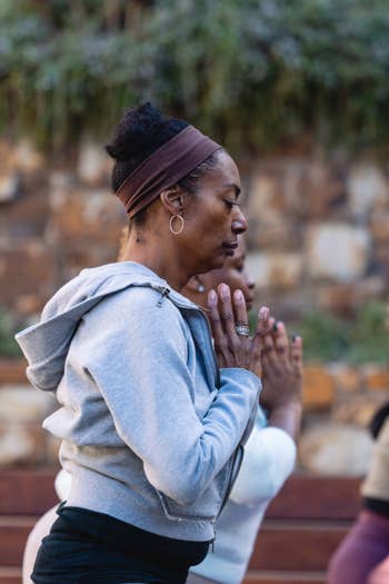 Woman in a headband claps hands while kneeling in outdoor group meditation, background blurred with seated people