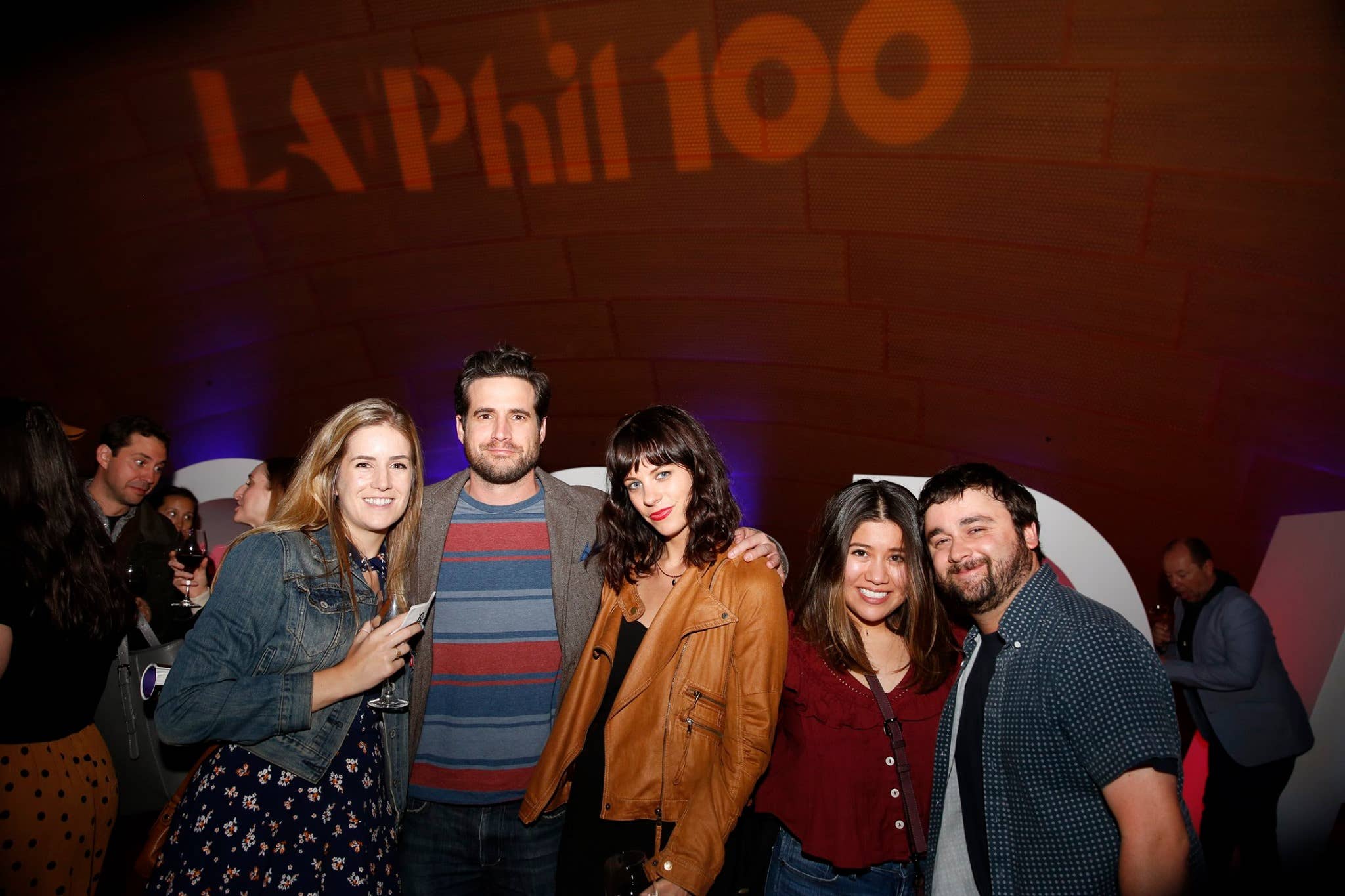 Group of five people posing at a nighttime event with “LA Phil 100” signage in the background.