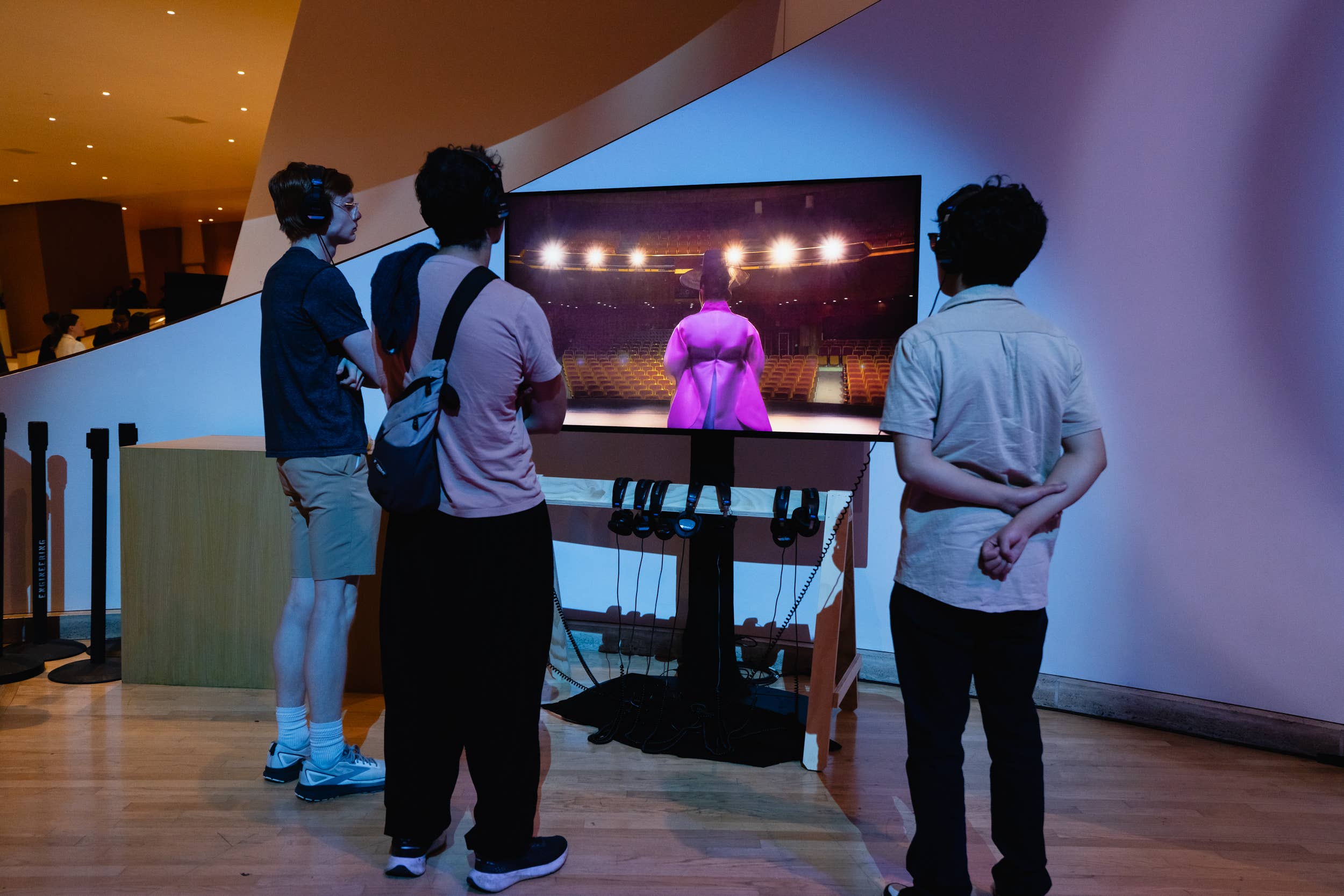 People wearing headsets stand at a console, watching a theater stage on a large screen at an exhibit.