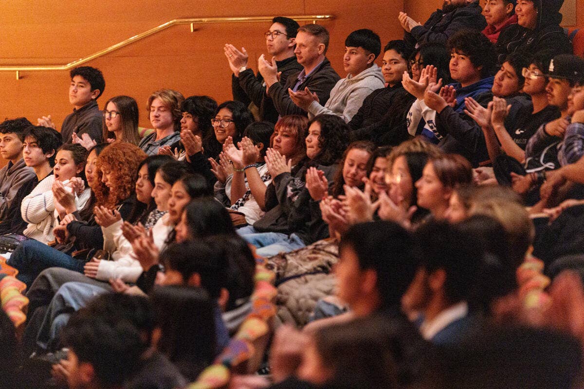 Students in an auditorium clap and cheer with raised hands during a school event.