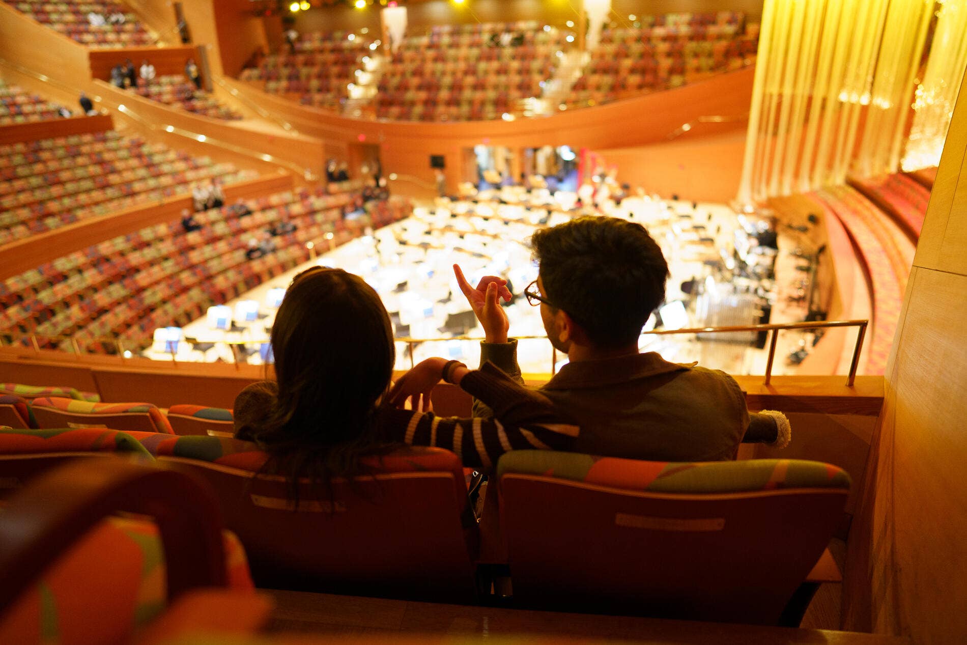 Man and child sit in theater seats, watching the stage in a warmly lit auditorium.