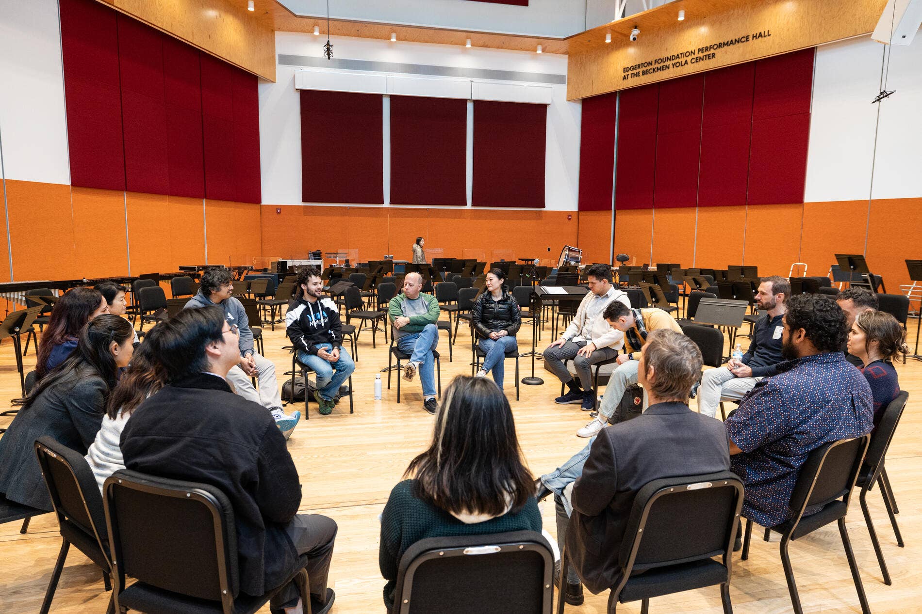 People seated in a circle during a meeting in Edgerton Foundation Performance Hall with red curtains and stage setup