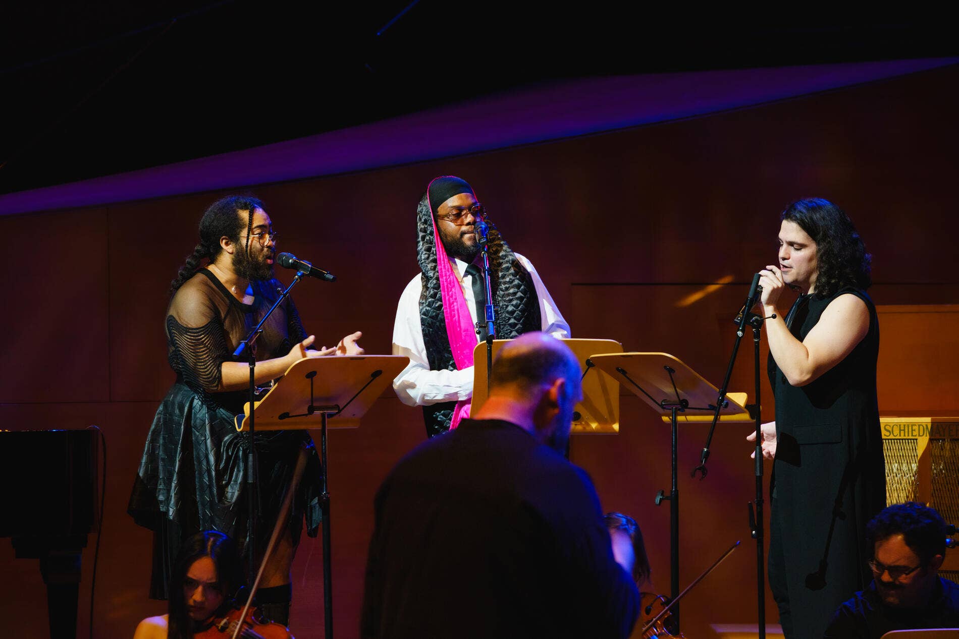 Three performers on stage with microphones, during a live music event.