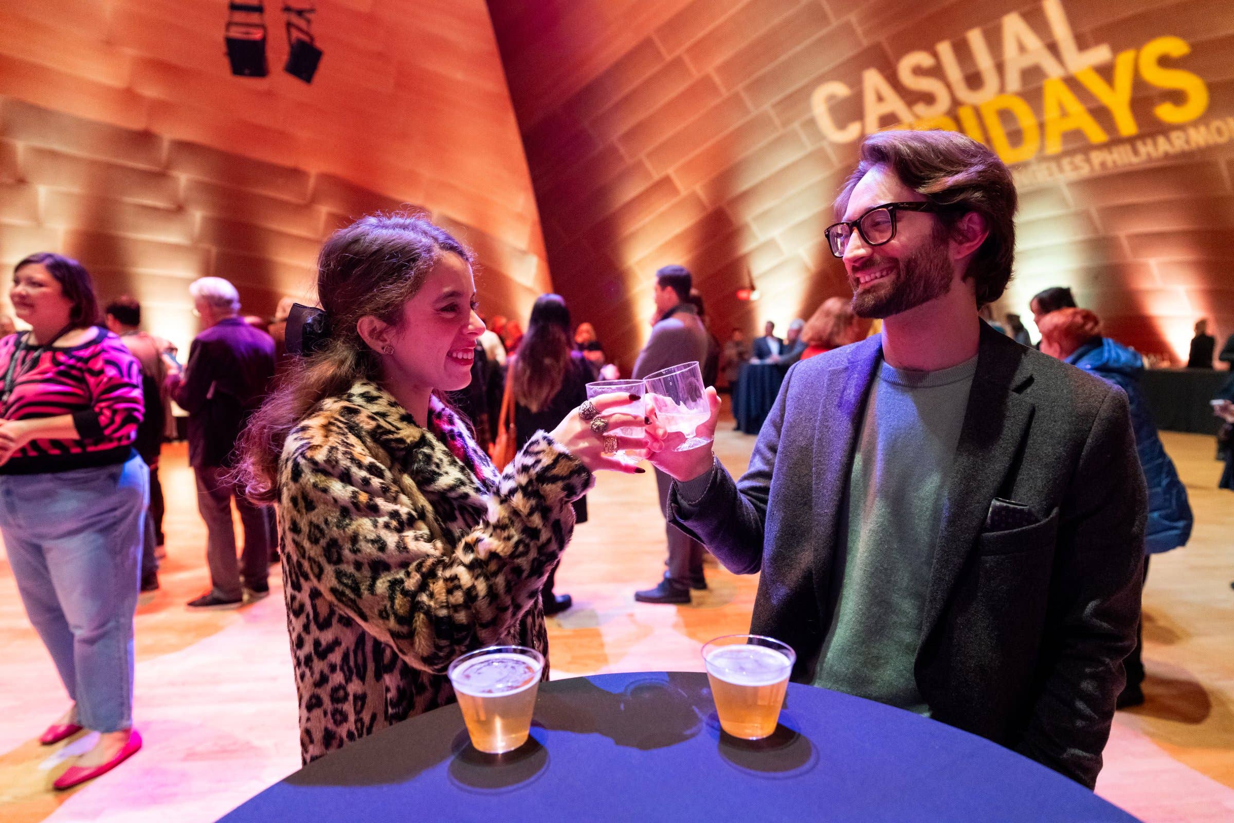 Smiling couple clink glasses at a conference with “Casual Fridays” banner in the background