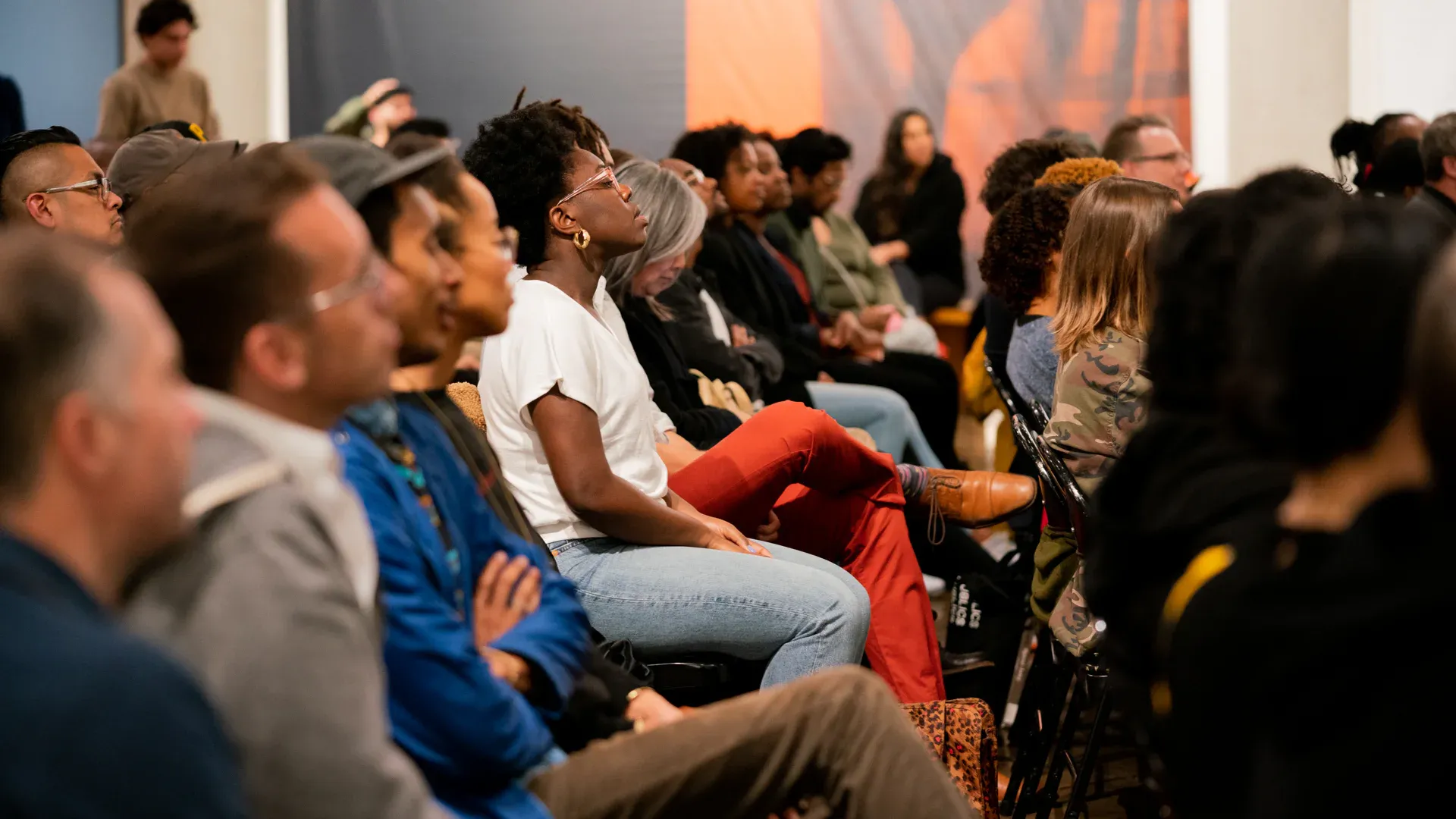 Audience seated in a conference hall, listening attentively while a speaker stage glows with warm sunset light.