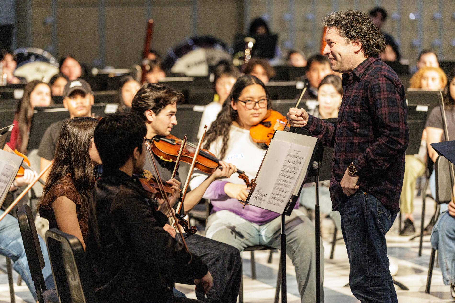 director de orquesta de pelo rizado director de orquesta una orquesta de violinistas en una sala de conciertos, sonriendo en medio de la actuación.