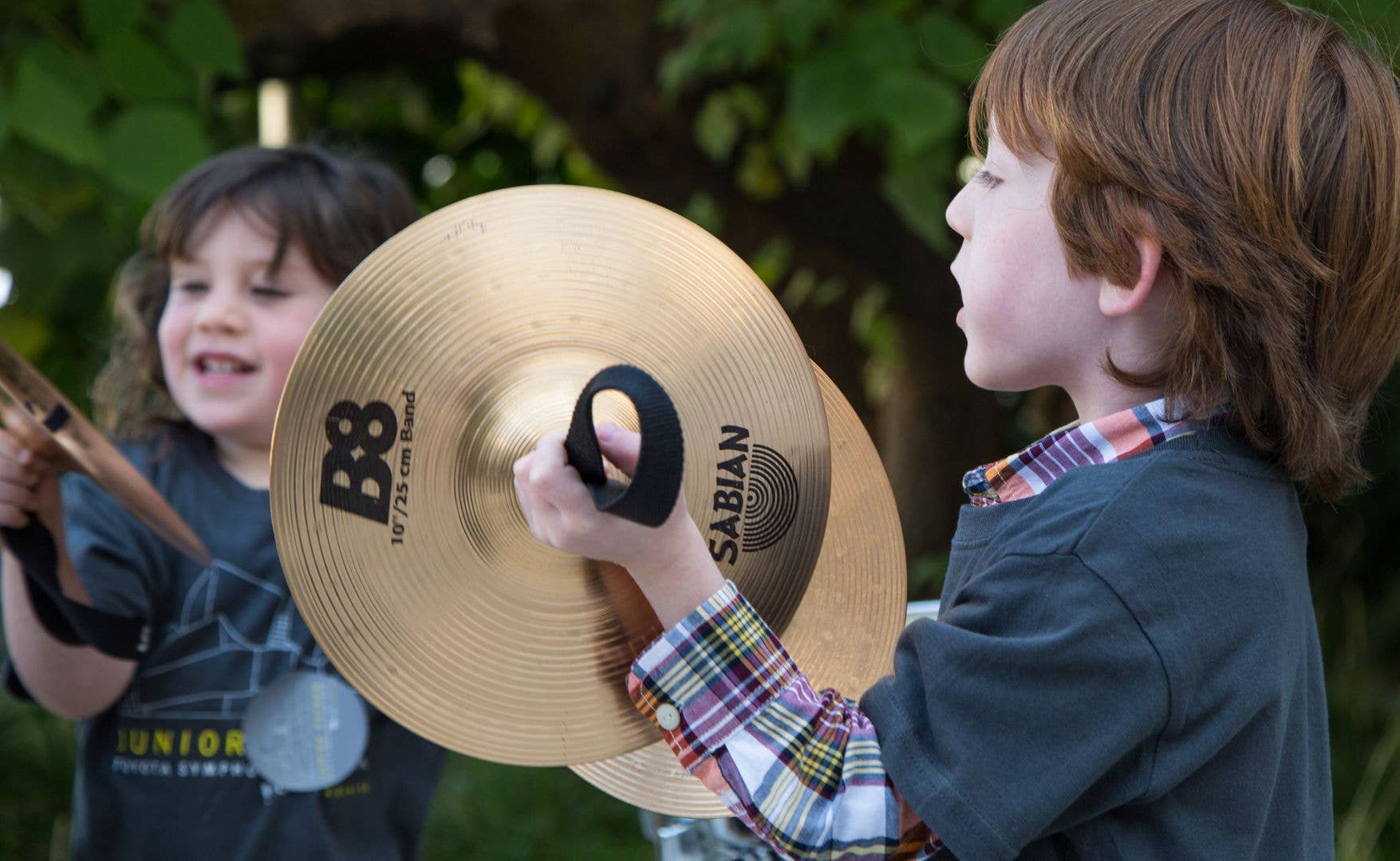 Two children outdoors, one holding a large “B8” cymbal-like disc while the other smiles nearby.