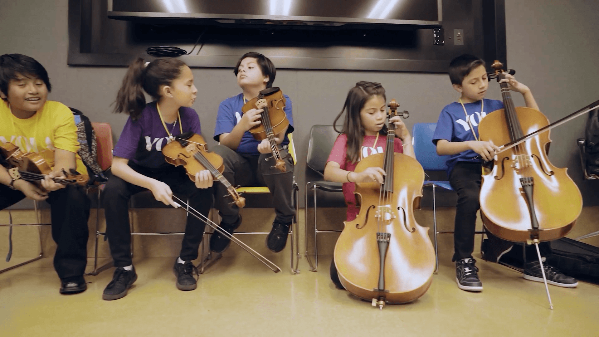 YOLA students practice their string instruments while waiting for class to begin.