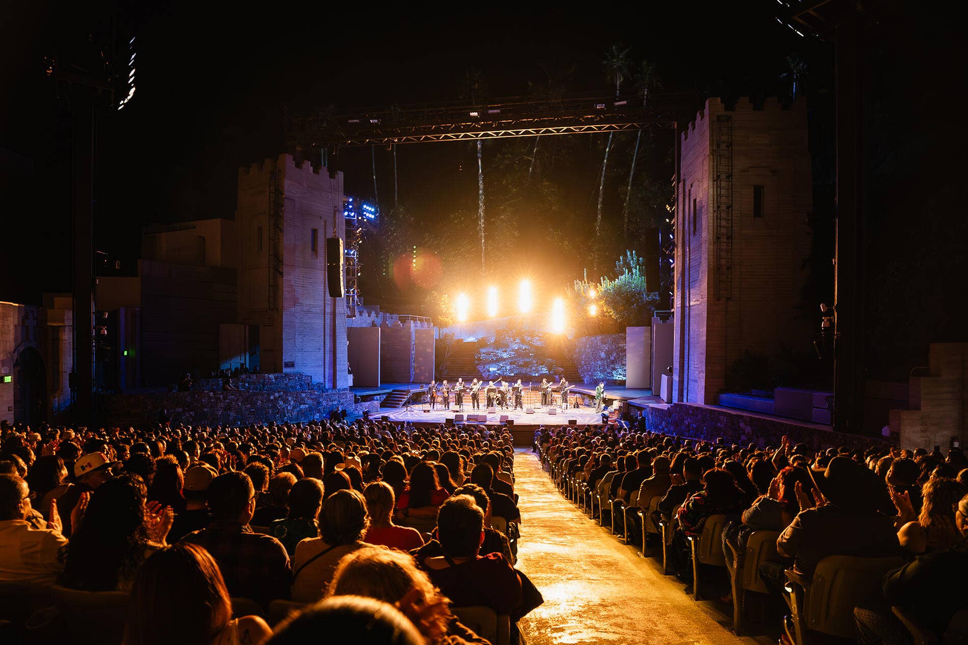 Crowd watches a nighttime concert stage with bright spotlights, fireworks and confetti, and fountains of sparks.