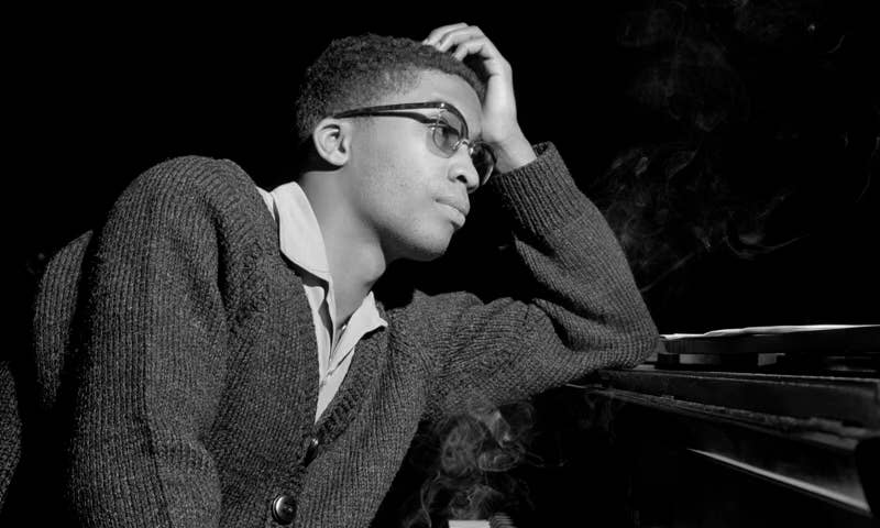 A black-and-white image of young Herbie Hancock leaning against a piano.