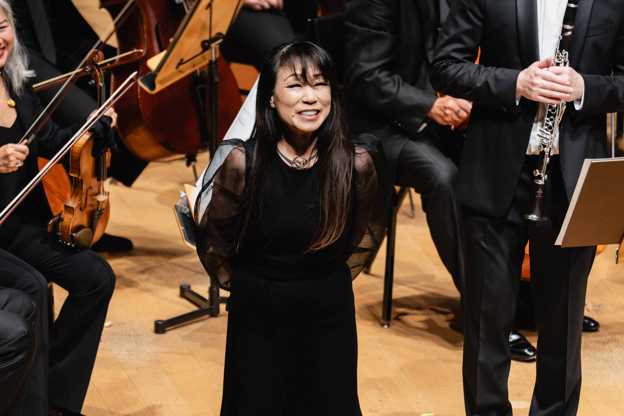 Smiling pianist conductor embraces on stage with clarinetist, cellists, and orange string instruments during performance
