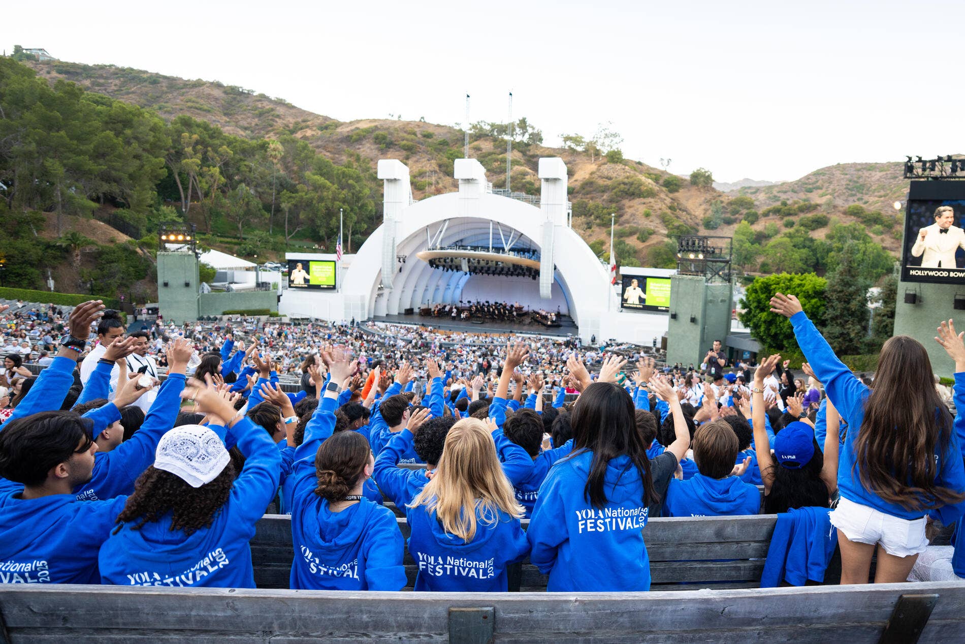 Los alumnos YOLA Nacional , vestidos con sudaderas azules a juego, se sientan emocionados entre el público del Hollywood Bowl durante una actuación.