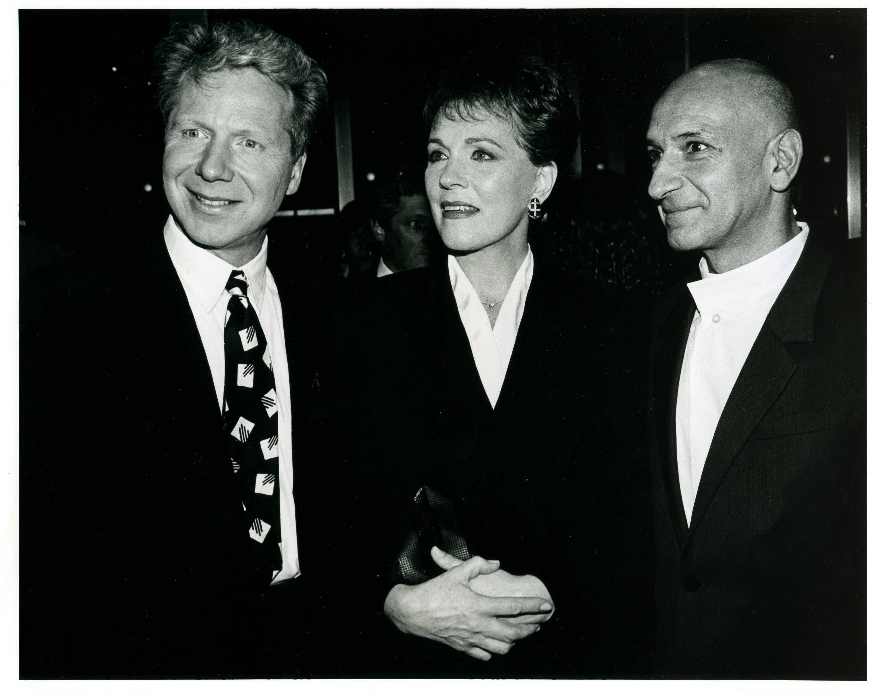 Three people in formal attire pose for a vintage black-and-white photo, smiling at the camera.
