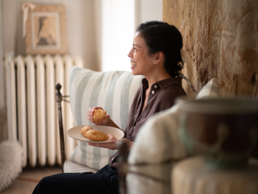 A woman sits, holding a plate, eating pastries from the plate.