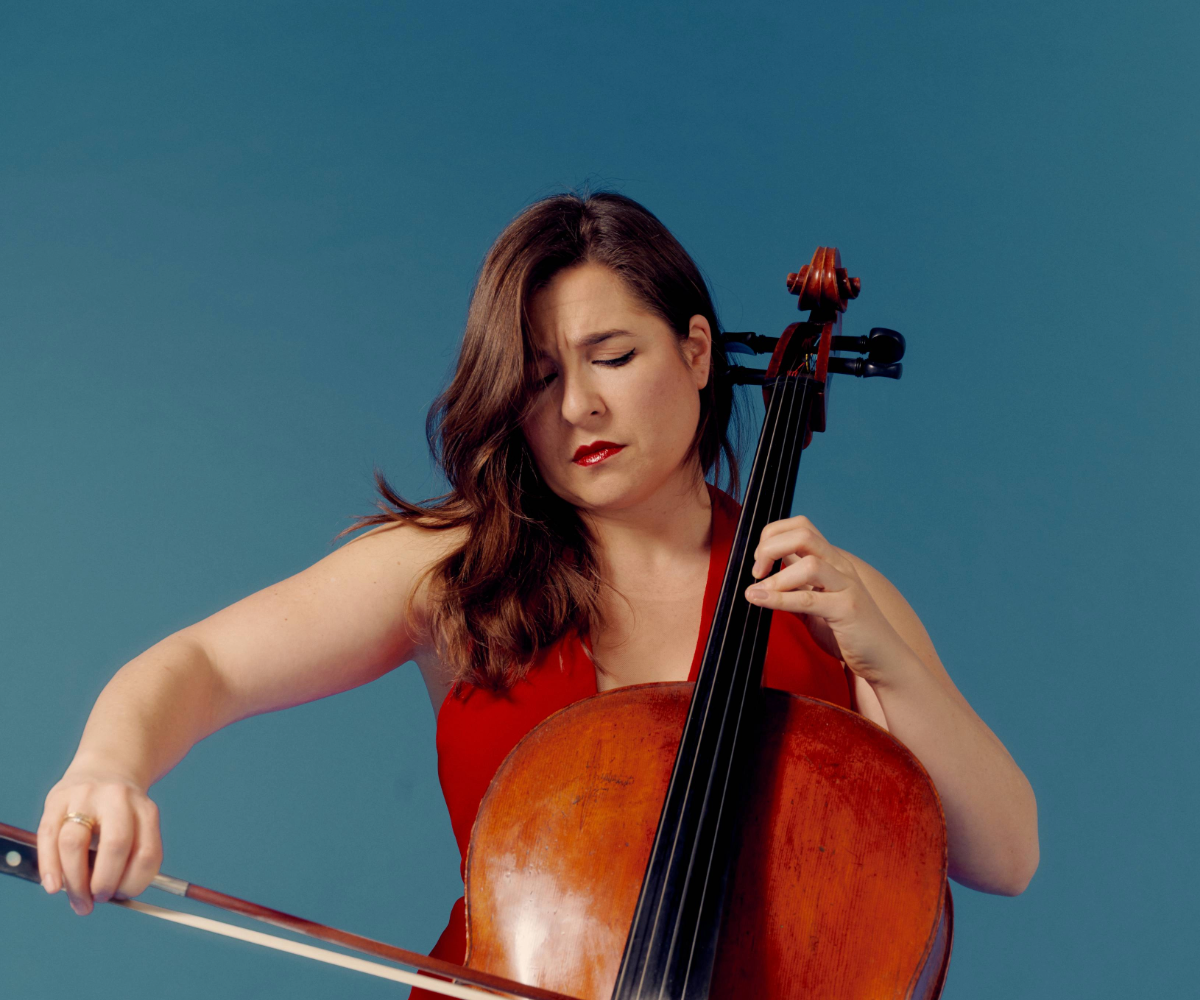 Una mujer con un vestido rojo tocando el violonchelo con los ojos cerrados sobre un fondo azul.
