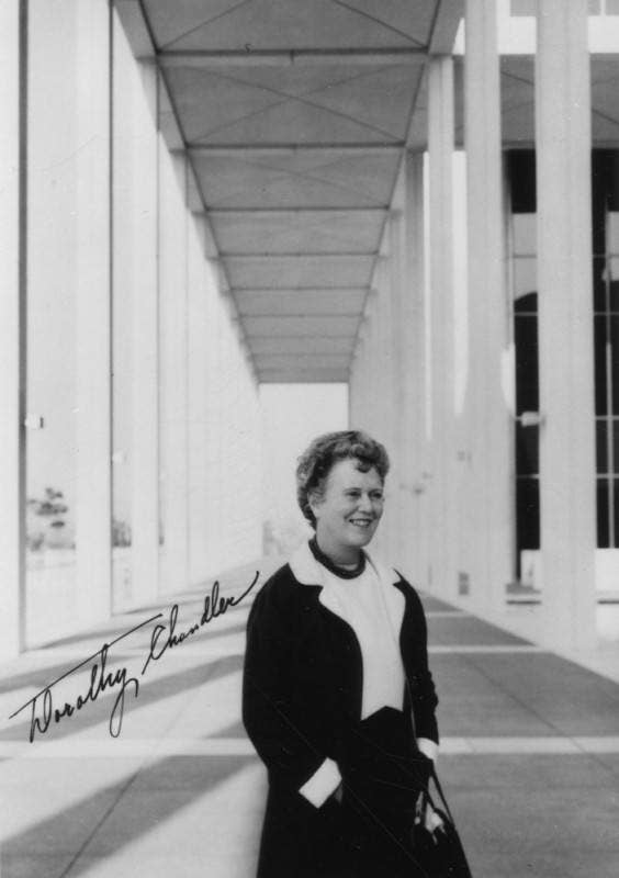 A black and white portrait of Dorothy Chandler seated outdoors, smiling at the camera.