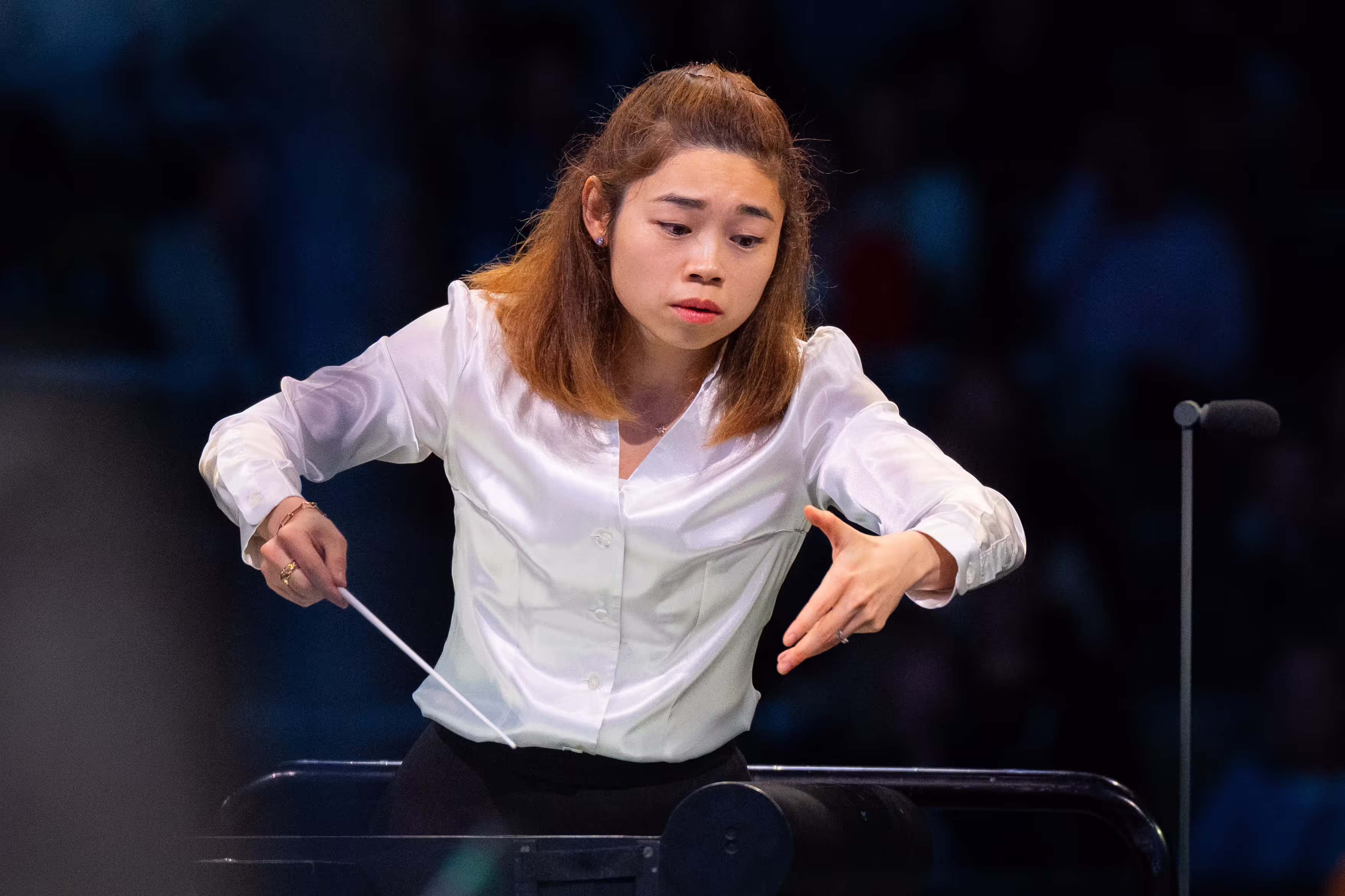 director de orquesta camisa blanca, concentrada, sosteniendo una batuta el brazo extendido