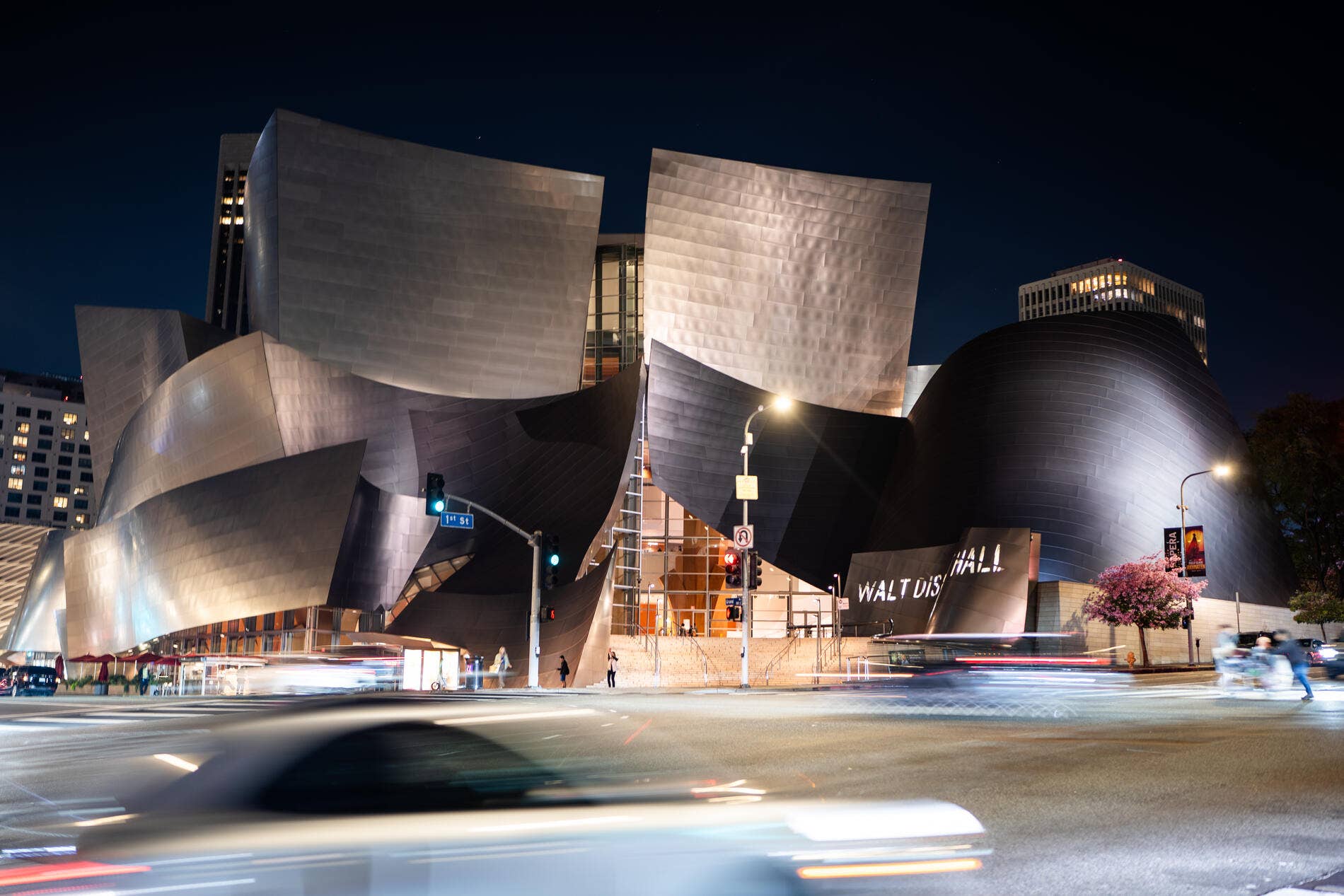 Walt Disney Concert Hall facade at night with curved metallic panels and light trails from passing vehicles