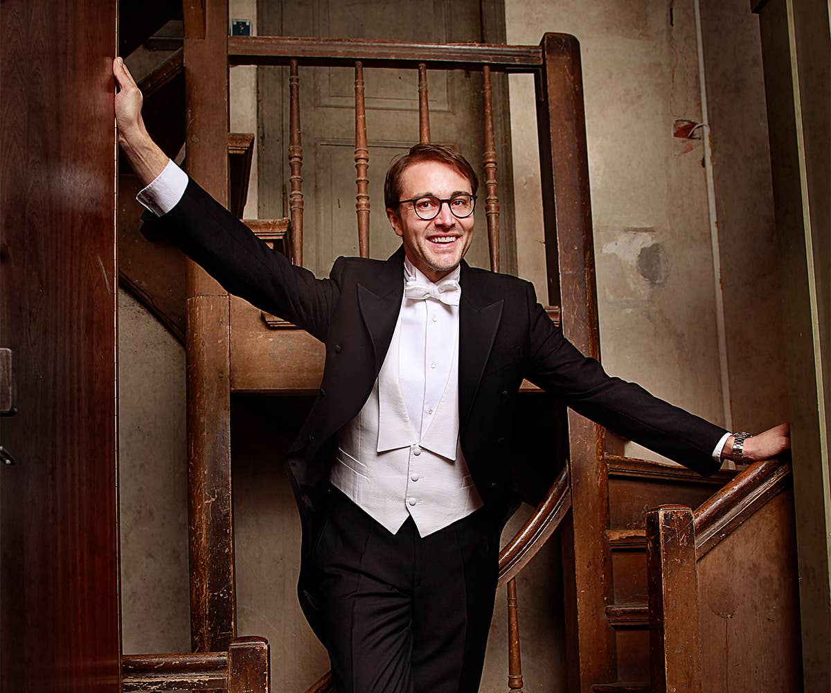 Christian Schmitt wearing a tuxedo stands in front of a staircase. 
