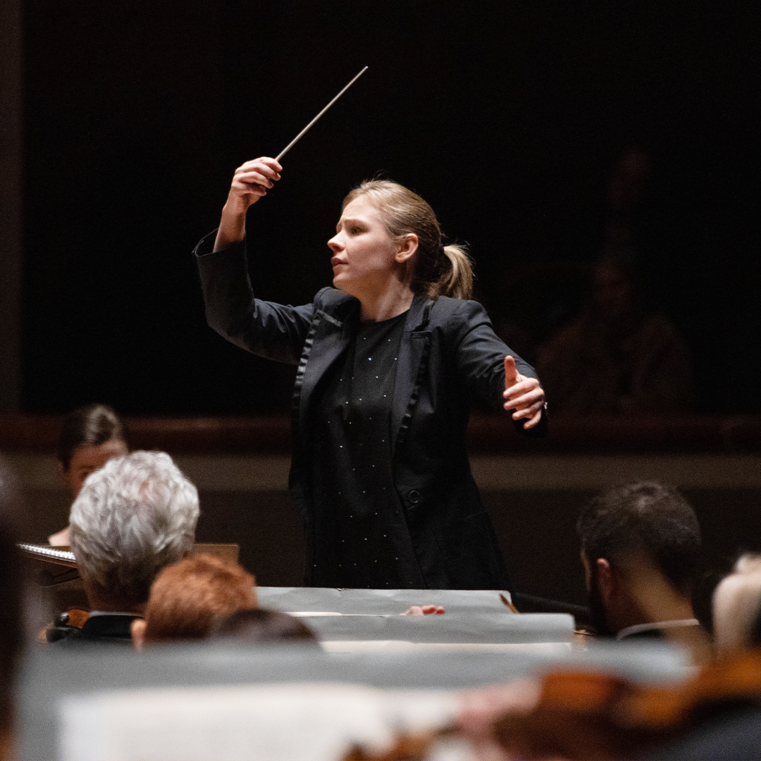 Gemma New raising a conductor's baton in her right hand.