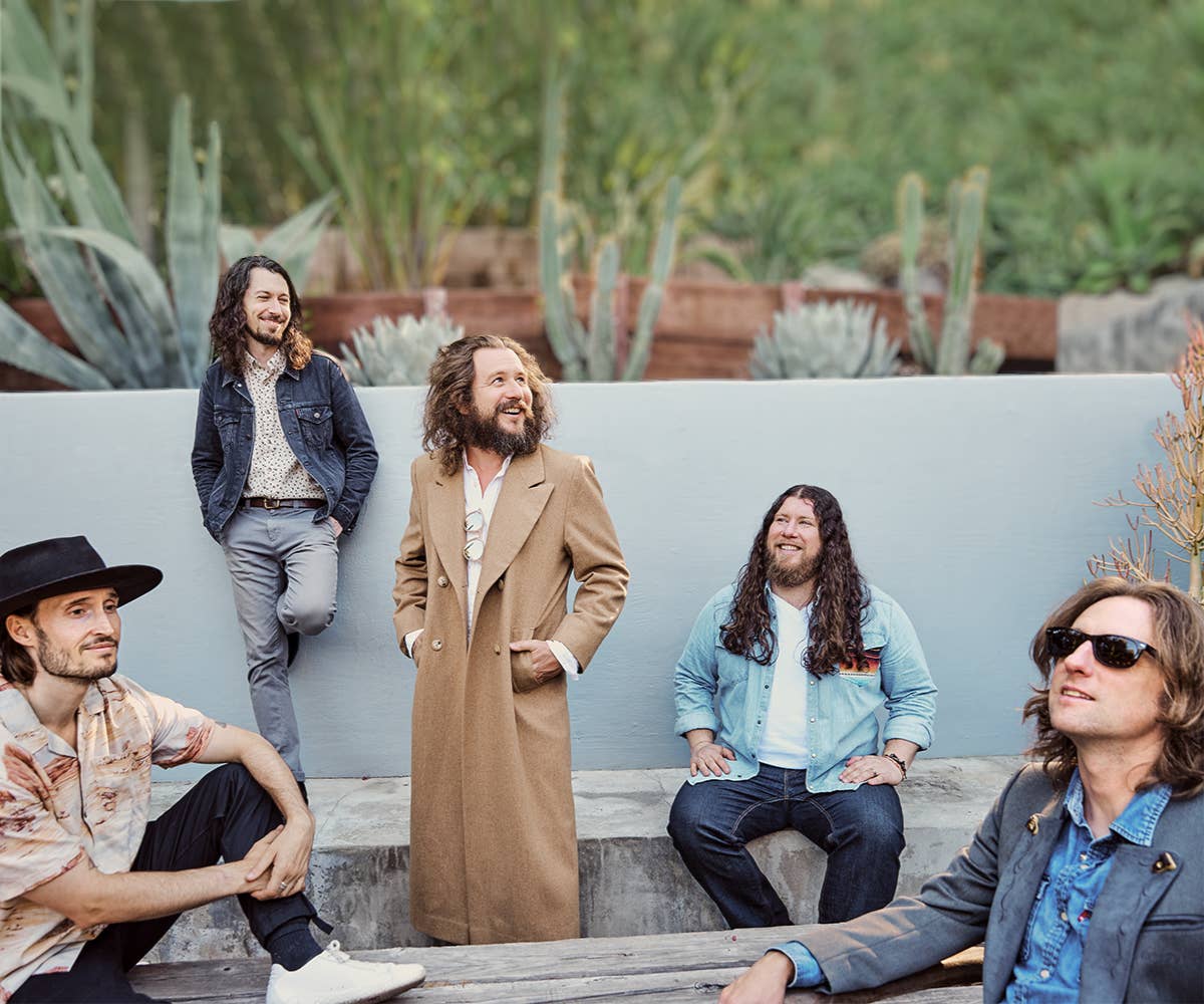 Smiling members of My Morning Jacket sit and stand in front of succulents and look up at the sky. 