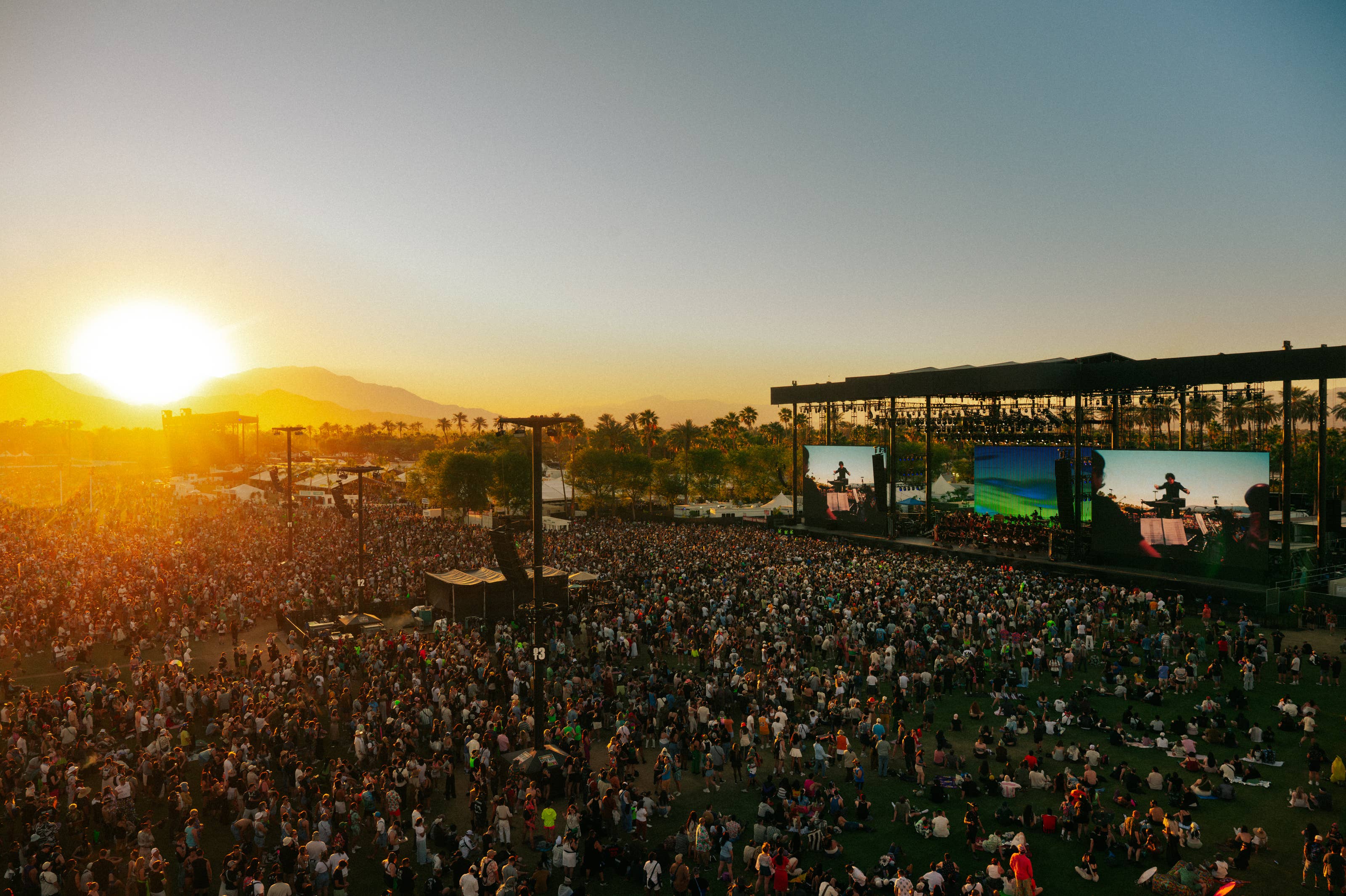 An aerial view of the crowd at Coachella watching the Los Angeles Philharmonic on stage at sunset.