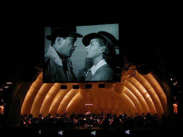 Large stage shows crowd as giant screens display two people talking from black & white movie under dramatic lighting