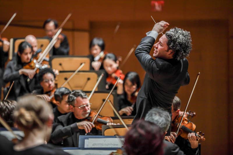 director de orquesta ambos brazos para dar la señal a los músicos durante un ensayo, con los violinistas sentados detrás de él.