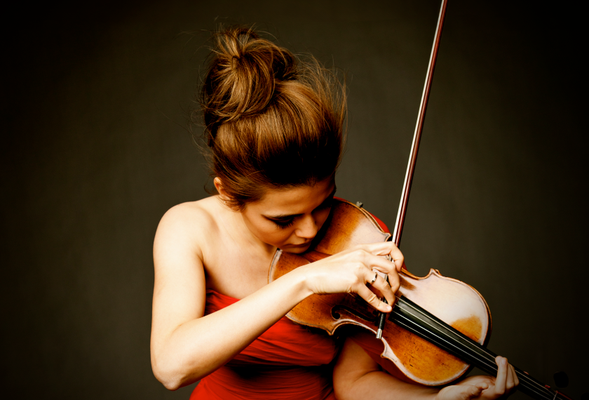 Woman in a red dress plays violin with intense focus against a dark background