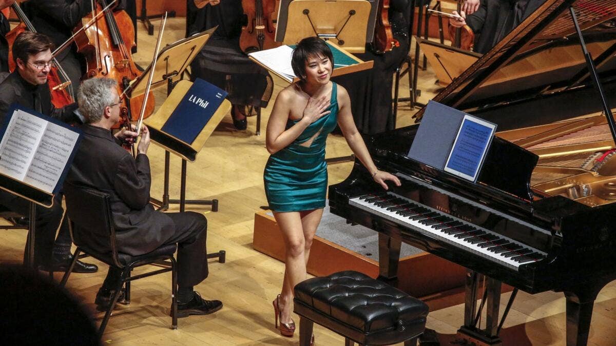Yuja Wang stands next to a paino, mid-bow, before beginning a performance with the Los Angeles Philharmonic orchestra.