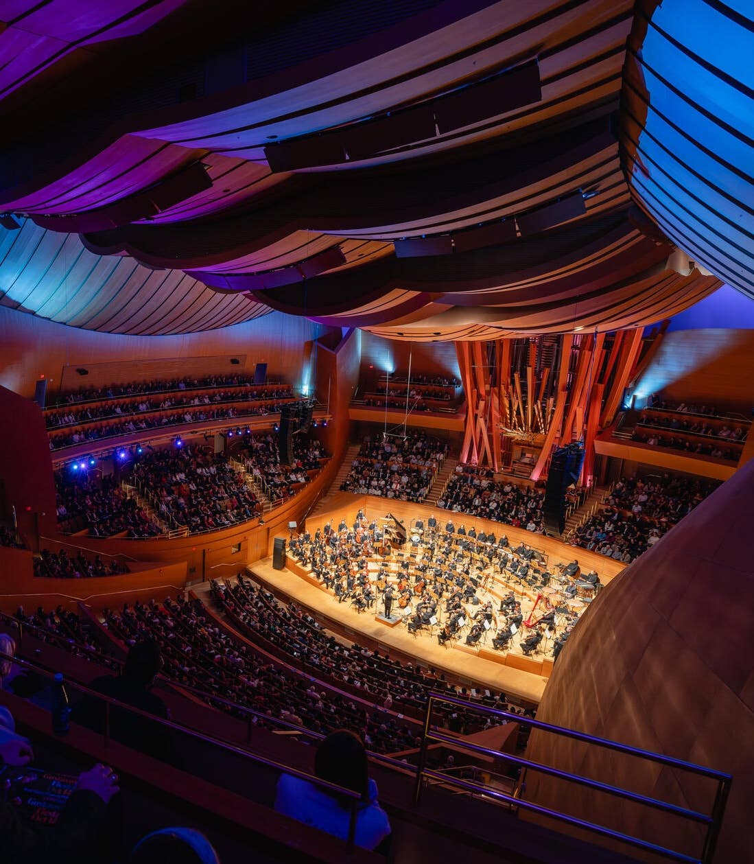 A wide image of audience members watching the Los Angeles Philharmonic Orchestra perform on stage at the Walt Disney Concert Hall.