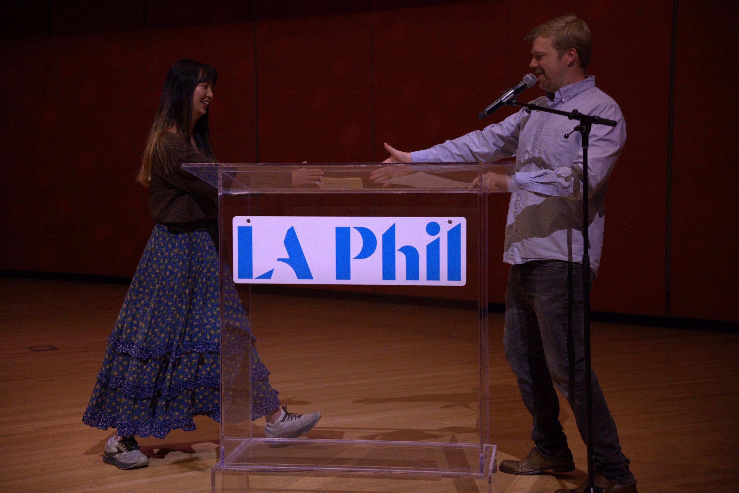 Man and woman at a podium with a microphone during a presentation, with “LA Phil” logo displayed on the lectern.