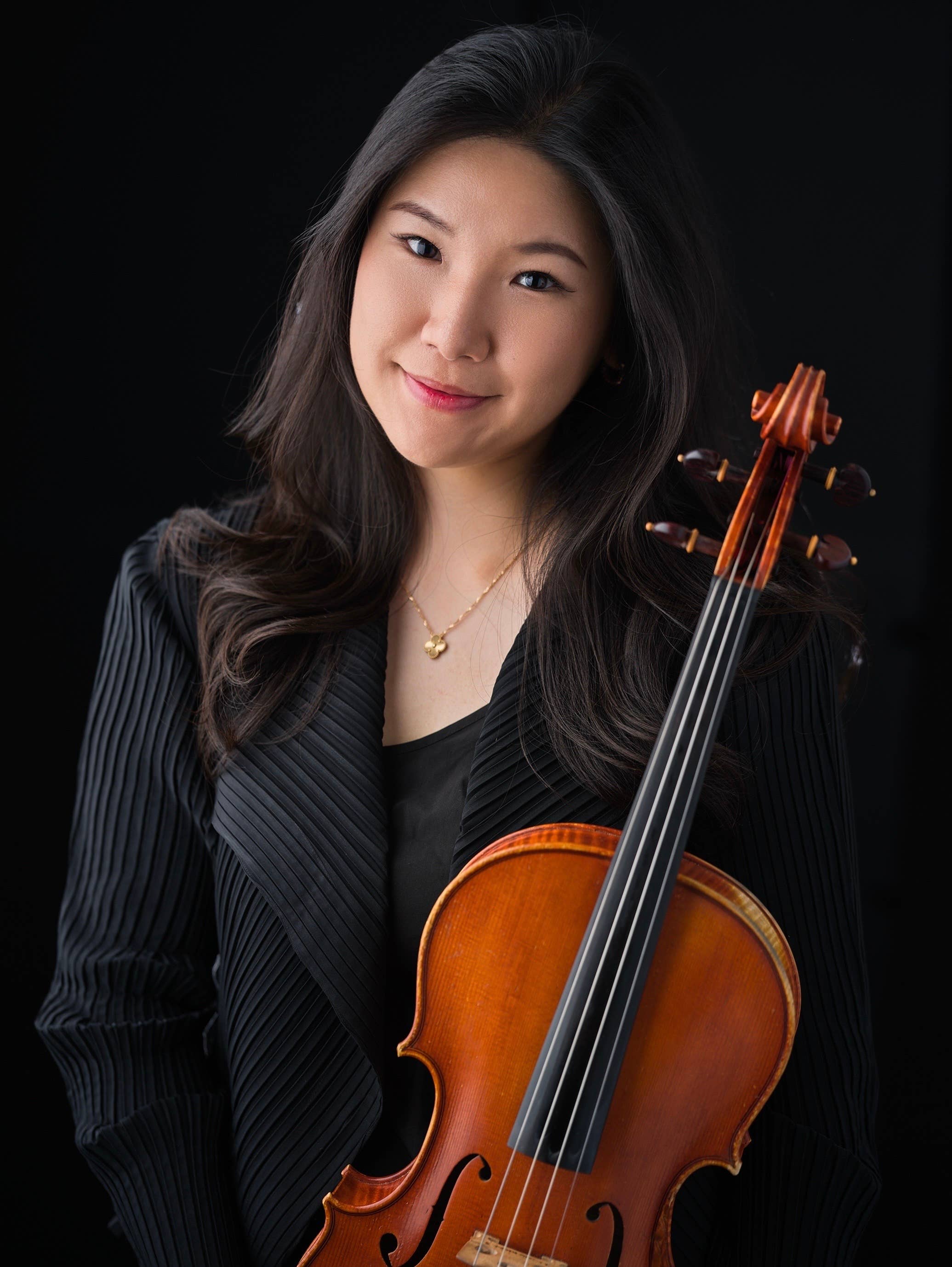 Portrait of a woman in a dark blazer holding an orange-brown violin on a black background