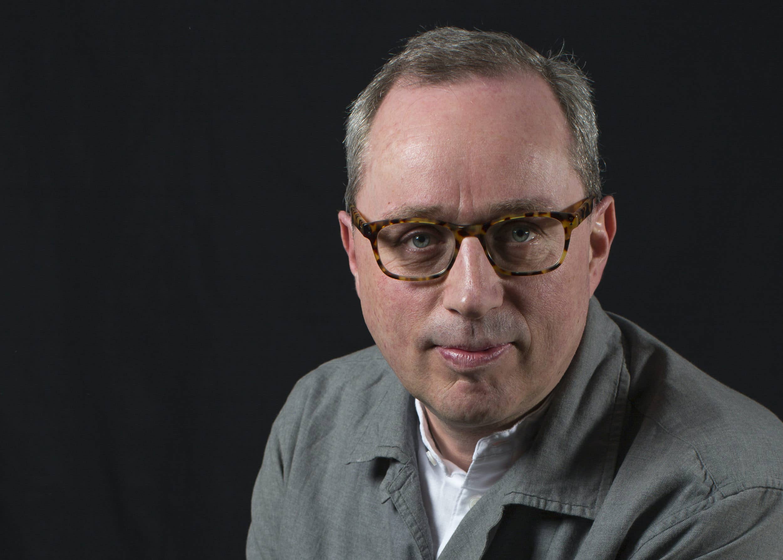 Close-up headshot of Christian Thompson wearing tortoiseshell glasses against a dark background.