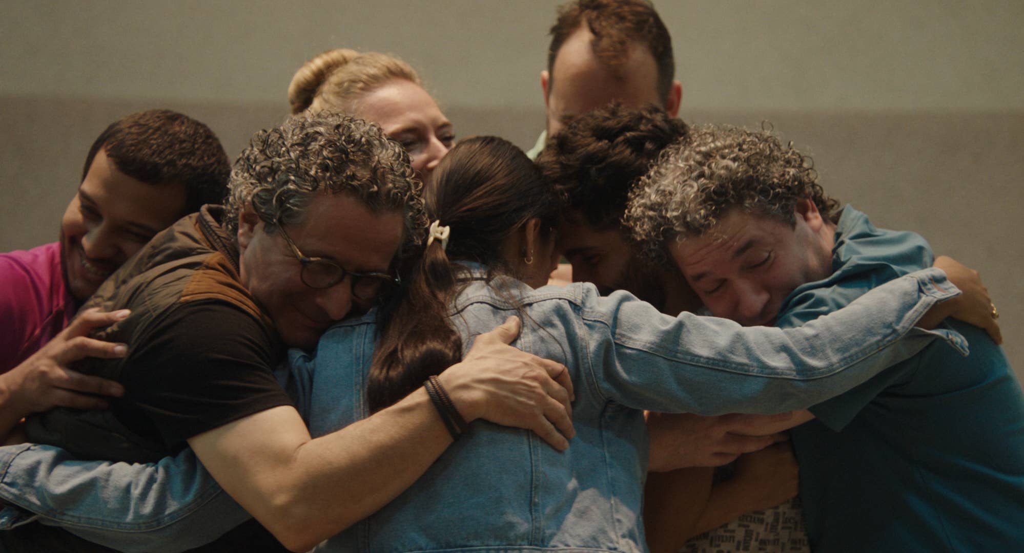 Group of performers hugging tightly, faces pressed together in an emotional group embrace indoors.