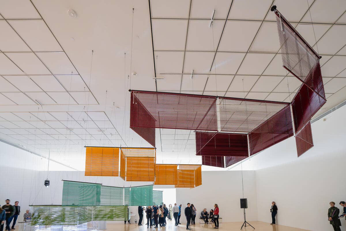 Interior of a bright exhibition hall with hanging red, orange, and green translucent installations in the ceiling overhead.