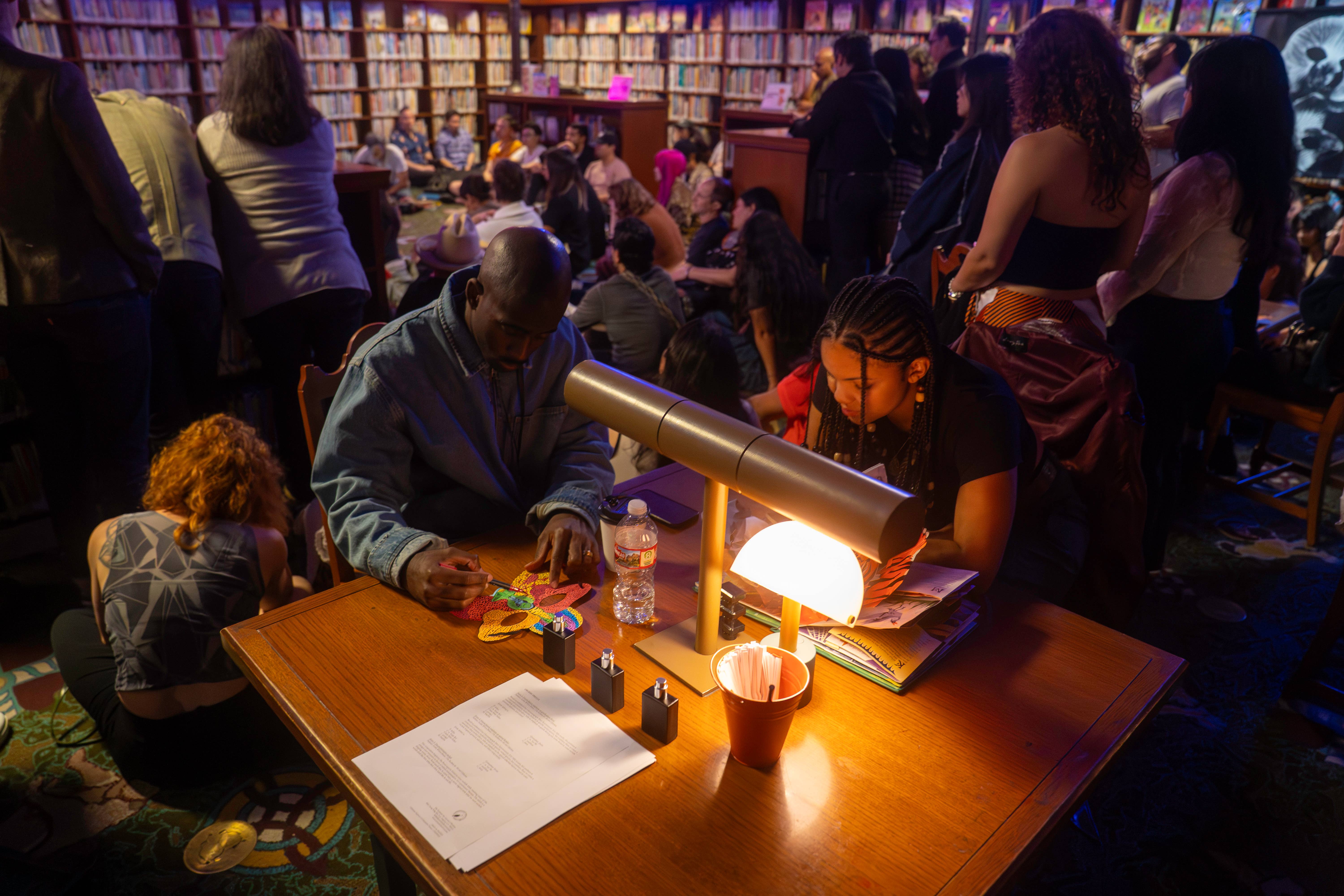Participants making art in a crowded, dark library space over a lamp-lit table