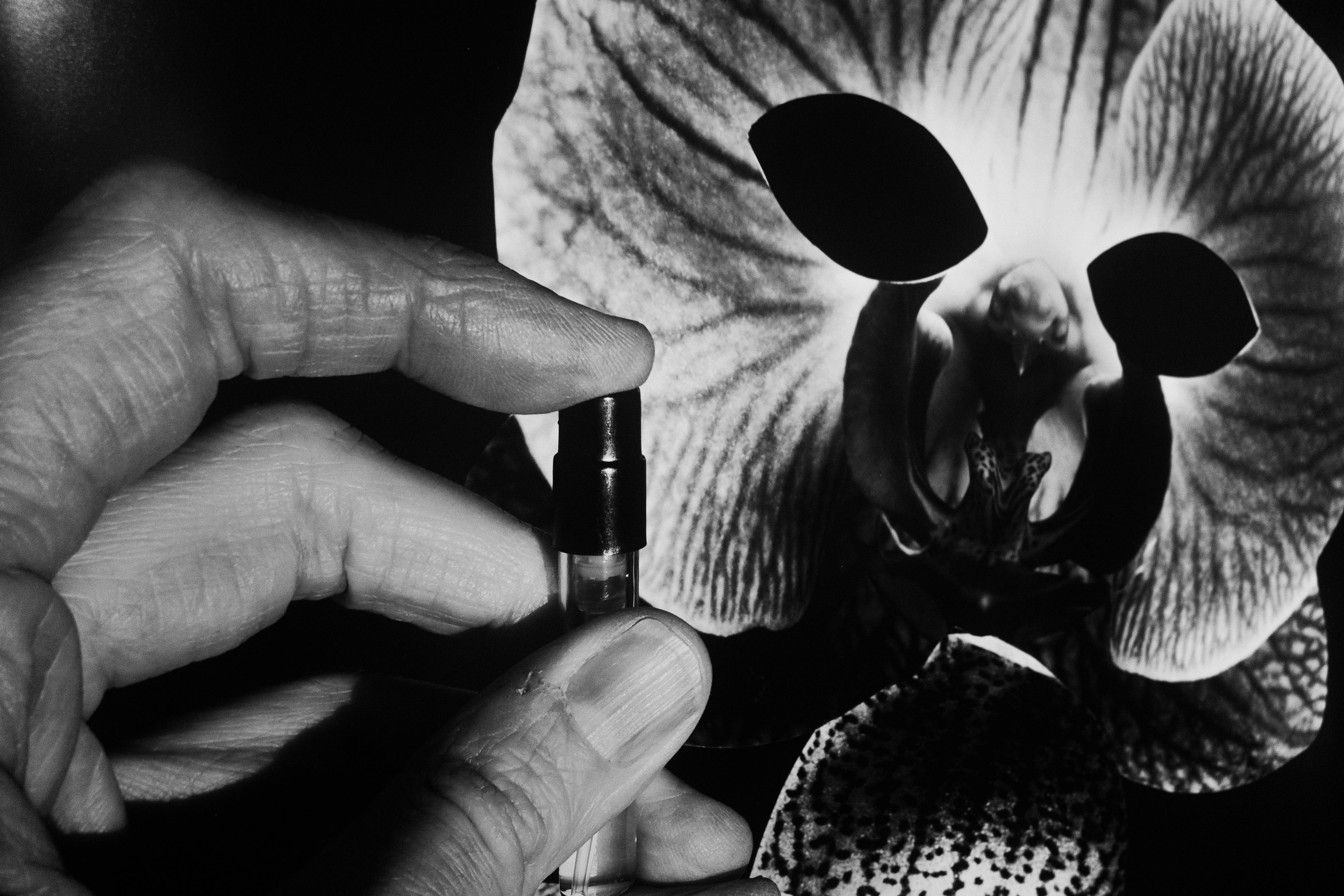 Black and white close-up photo of a hand spraying fragrance at an orchid mask