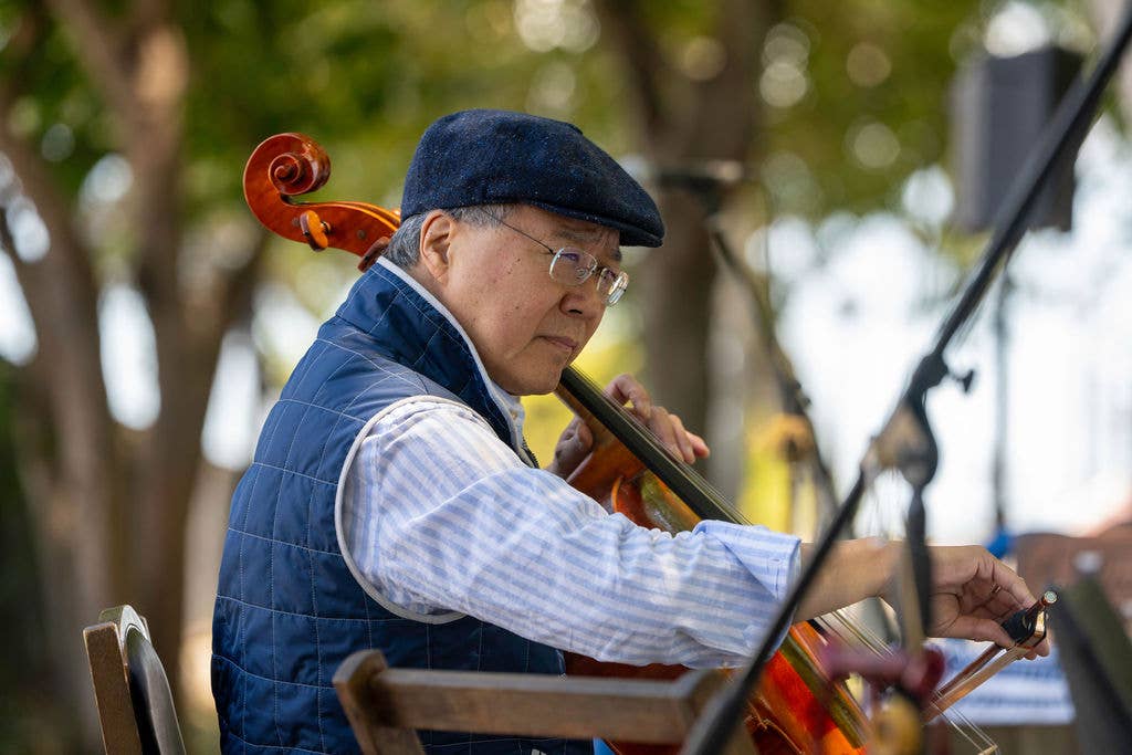 Yo-Yo Ma in a blue beret and blue outfit playing cello outdoors