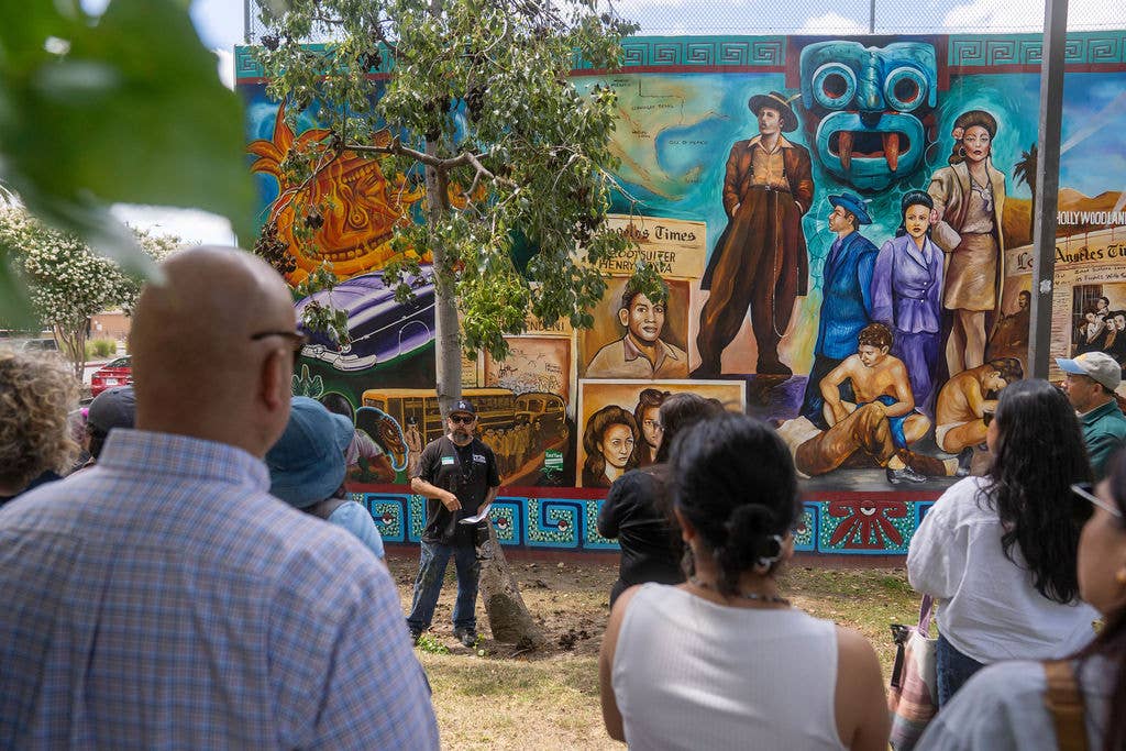 Crowd surrounding a mural depicting figures, the LA Times, and the Hollywood Sign