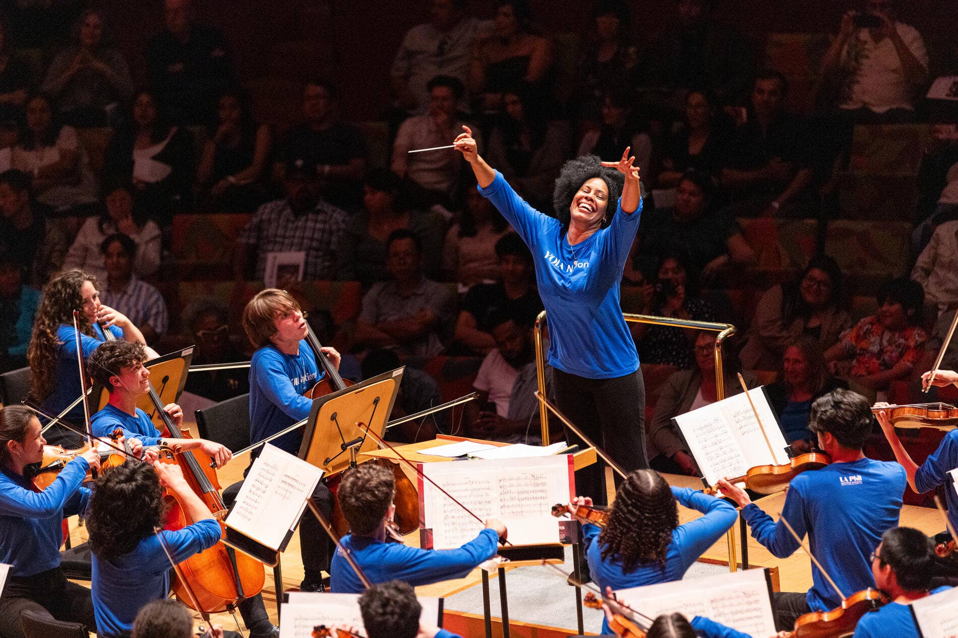 Jesscia Rivero Altarriba conducting a YNF ensemble with arms raised, audiences behind her.