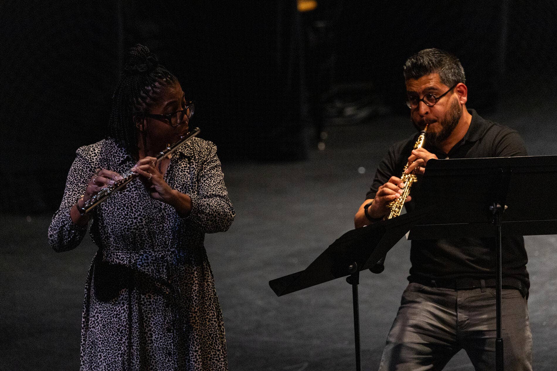 A flutist and a clarinetist faculty member perform on a dark stage with music stands in front of them.