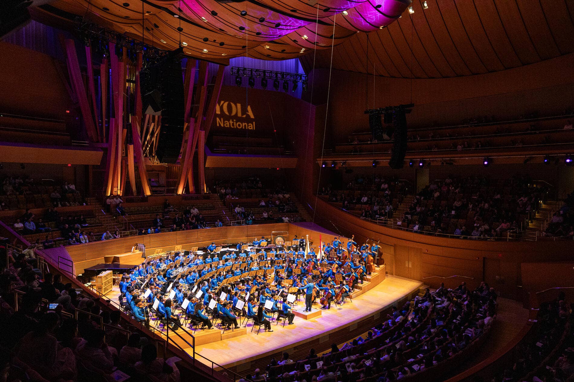 A full youth orchestra dressed in blue on the stage of Walt Disney Concert Hall